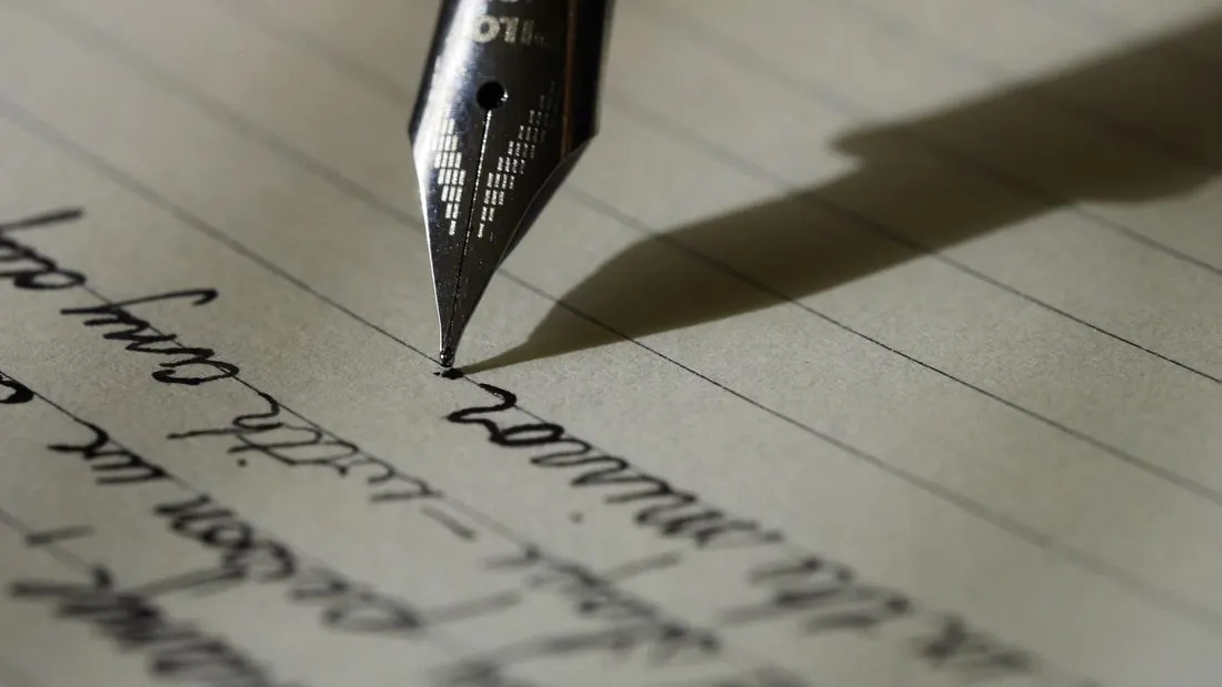 A close view of a fountain pen nib writing cursive handwriting on lined paper.