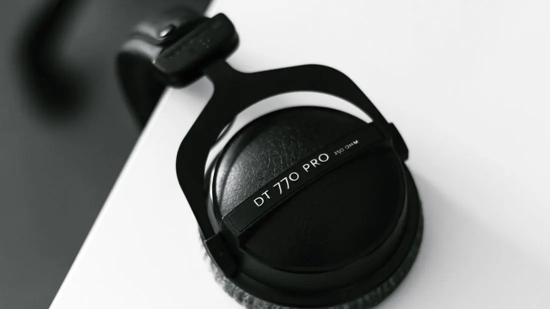 Black over-ear studio headphones resting on the edge of a white desk, seen from above.