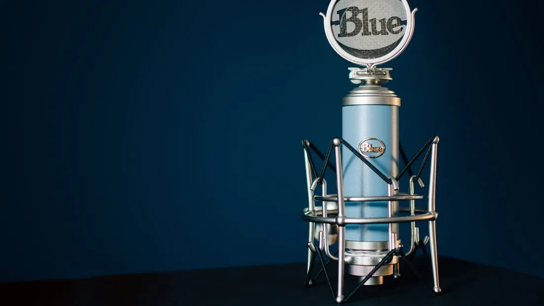 A pale blue condenser microphone in a metal shock mount against a dark blue background.