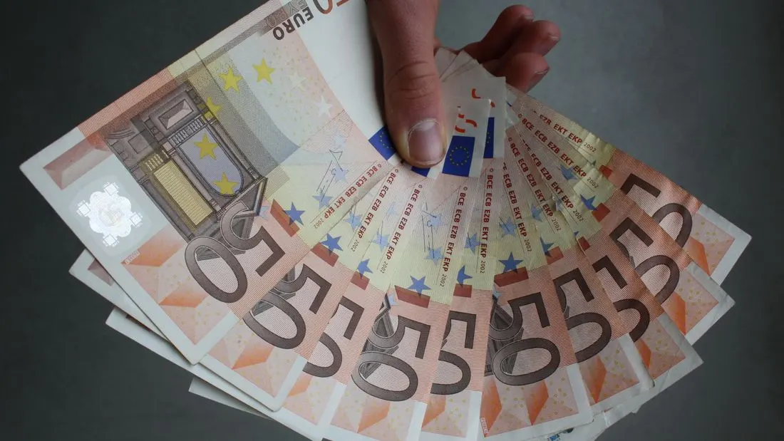 A hand holding a fan of fifty-euro banknotes against a grey background.