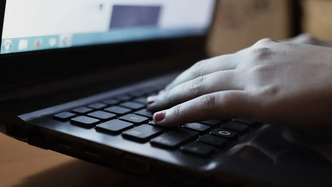 A hand resting on the keyboard of a dark laptop.