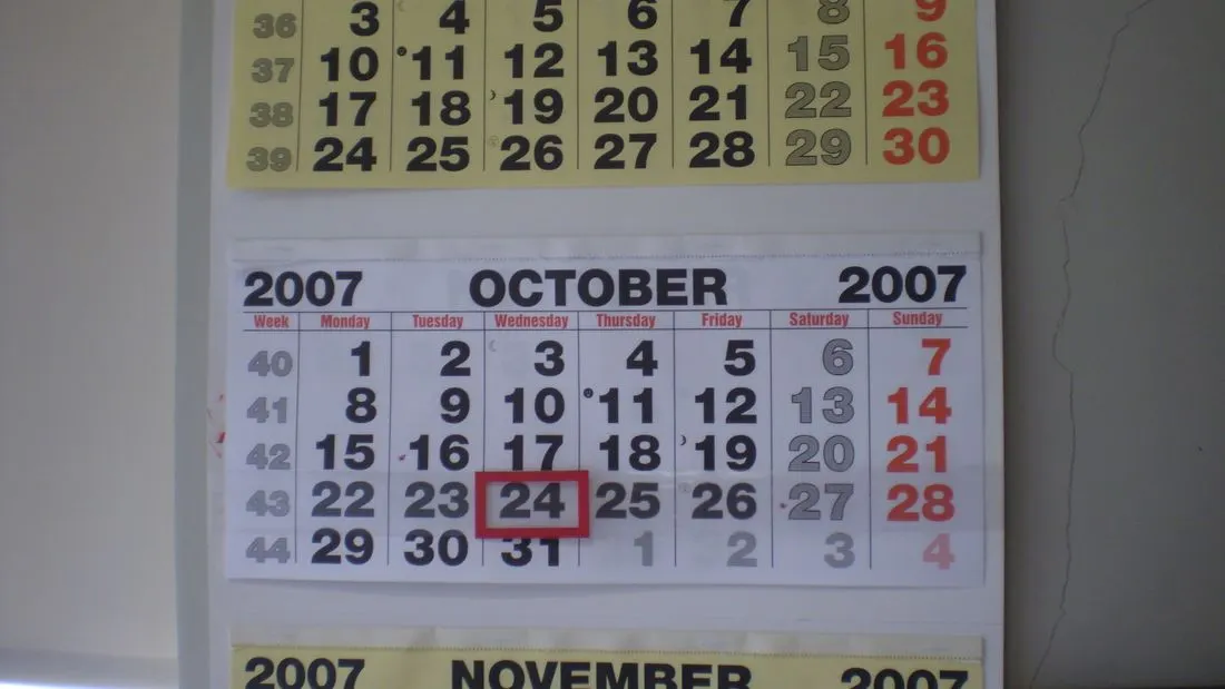 A paper wall calendar open at October with one date boxed in red.