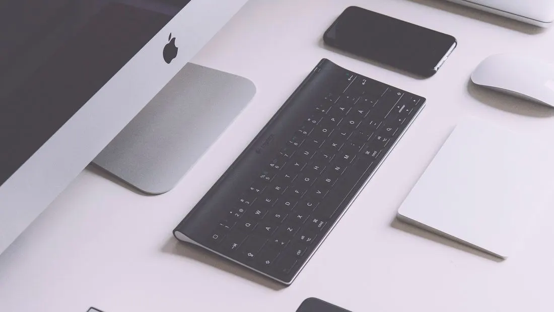 A desk seen from above with the edge of a monitor, a wireless keyboard, a phone, a mouse and a trackpad.
