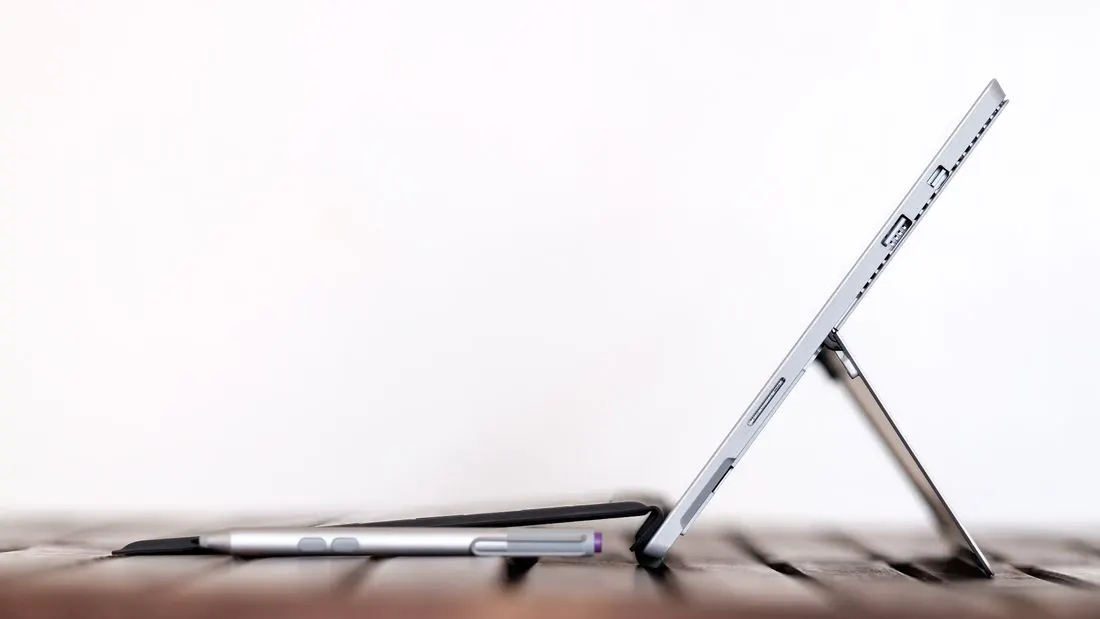 A tablet on a keyboard cover seen from the side, with a stylus lying in front of it.