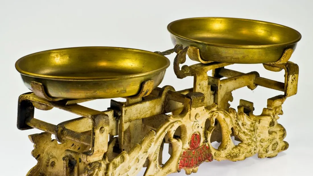 An old brass and cream cast-iron balance scale with two empty brass pans on a white background.