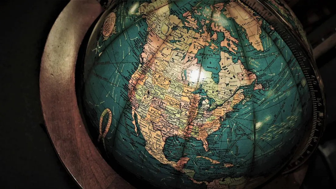 An old world globe in a wooden stand, turned to show North America in blue, cream and orange.