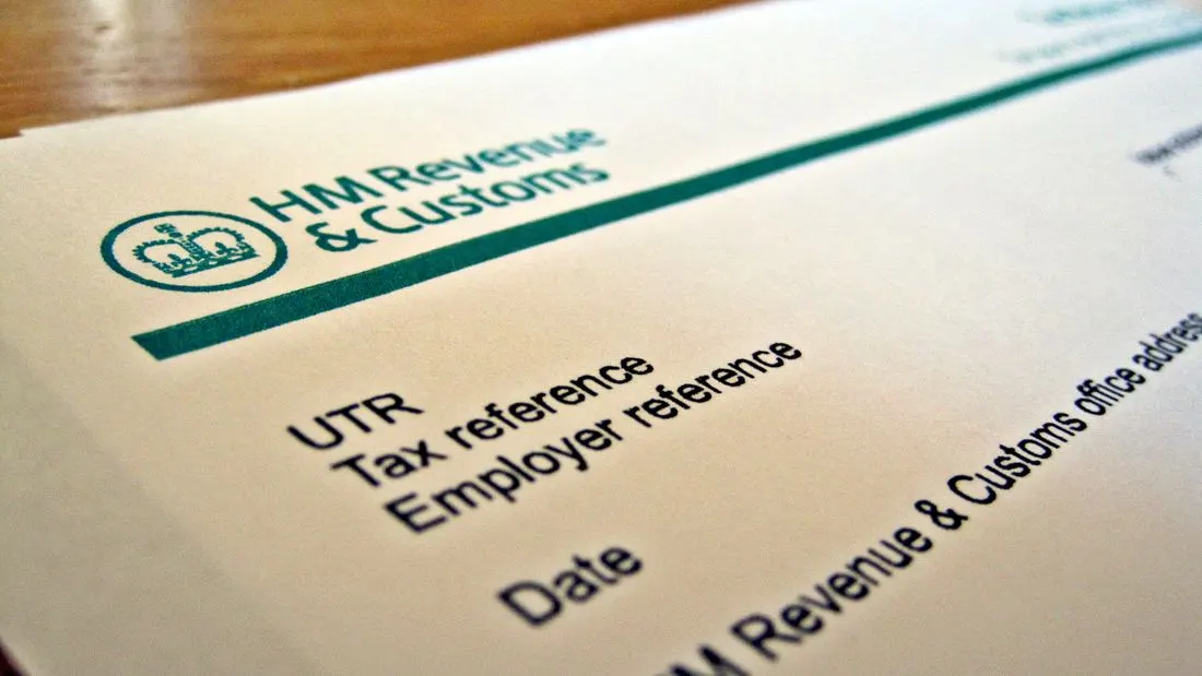 A close-up of a printed HM Revenue and Customs form on a wooden table, showing the department logo and the labels for tax reference and date.