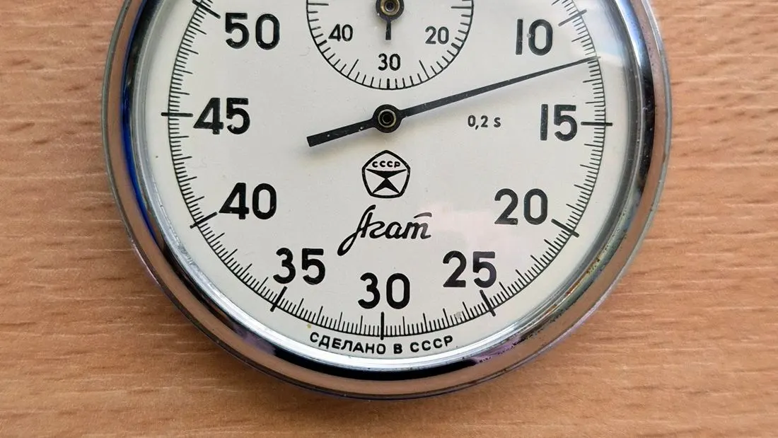 The dial of an old stopwatch with a black second hand, numbers from 5 to 60 and the Russian words for made in the USSR.